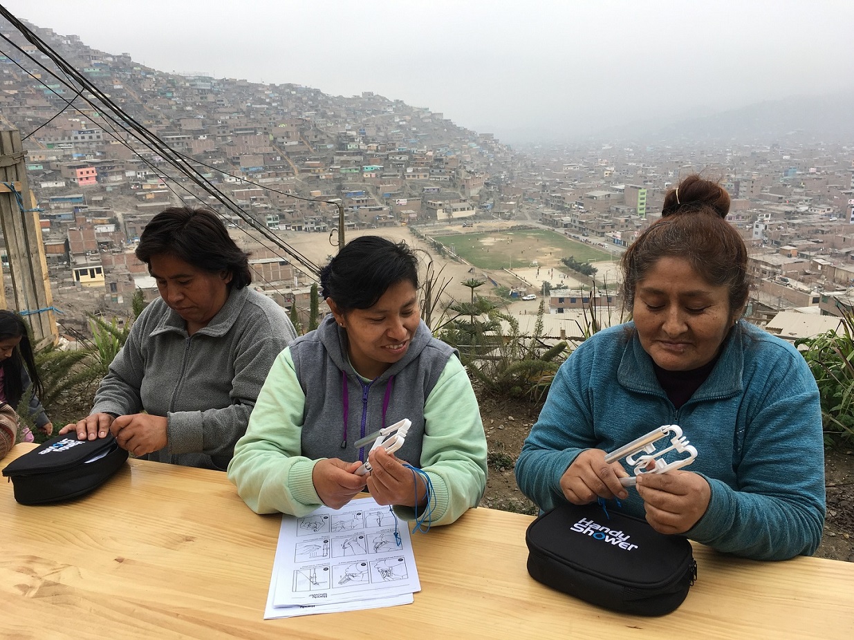 Trzy kobiety w średnim wieku siedzą na zewnątrz przy stole, w tle widać kotlinę, a powyżej niej wzgórze z zabudowaniami