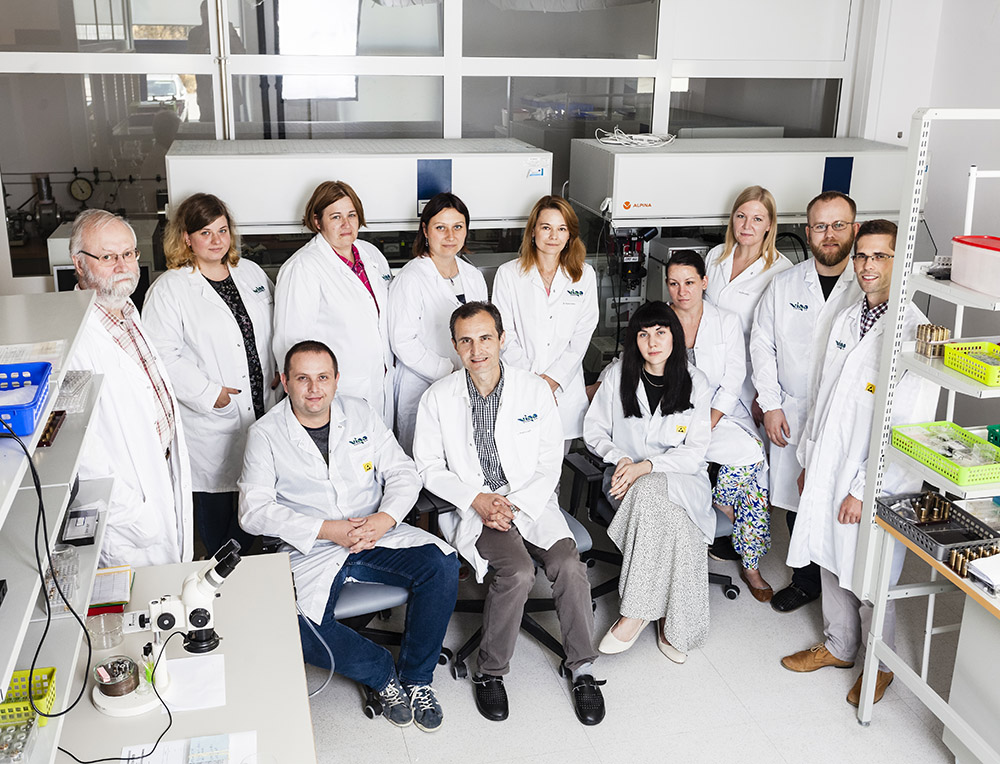 grupa kobiet i mężczyzn w różnym wieku ubrana w białe fartuchy przebywa w laboratorium